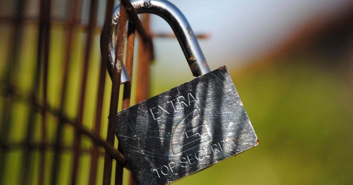 An open metal padlock hanging on a rusty fence, with the words Extra Top Security engraved on it: before entrusting money to a platform you check who is behind it