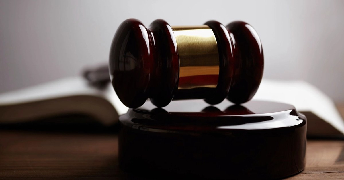 A dark wooden judge's gavel with a gold band, resting on an open book: trading is legal, but within precise rules