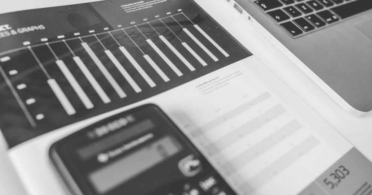 A calculator resting on a sheet with bar charts next to a laptop: trading online is worth it only after you have done the maths on costs